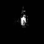 Black and white photo capturing a silhouette of a man walking in a dimly lit alley.